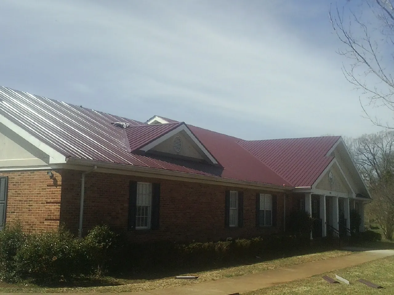 Red metal roof with gabled entries on a long brick building, from a Hail Damage Roof Repair job in Oak Run