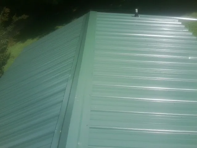 New green metal panels meeting at the ridge of a roof — Flat Roof Repair work by our crew in Oak Run