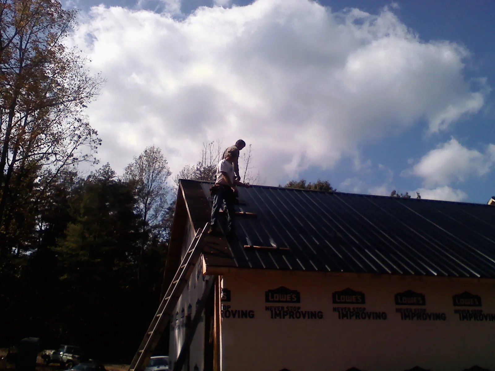 Roofer fastening dark metal panels high against a cloudy sky, from a Roof Inspection job in Oak Run