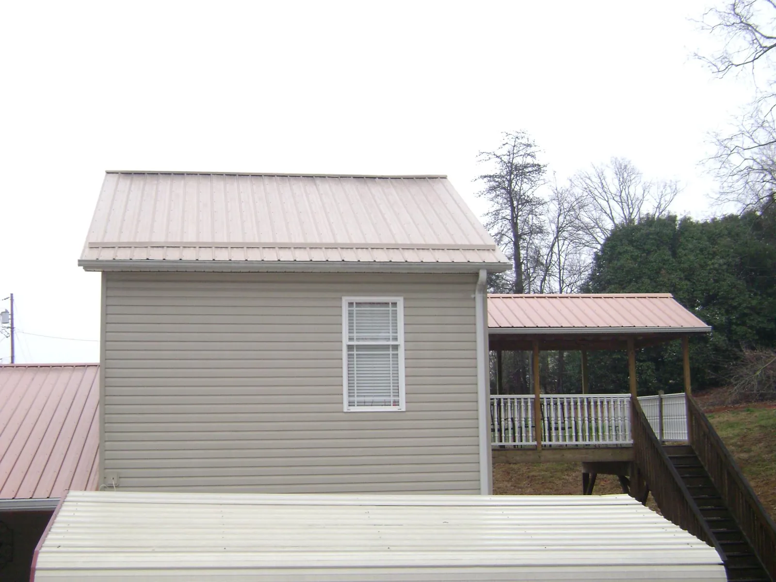 Tan metal roofs on a two story addition and attached porch, from a Roof Replacement job in Oak Run